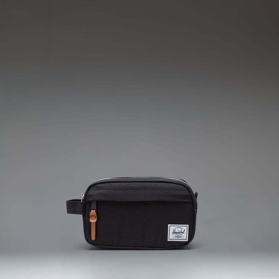 Herschel Supply Co Chapter Small Travel Kit in black, showing the compact toiletry bag with its side handle and classic woven label.